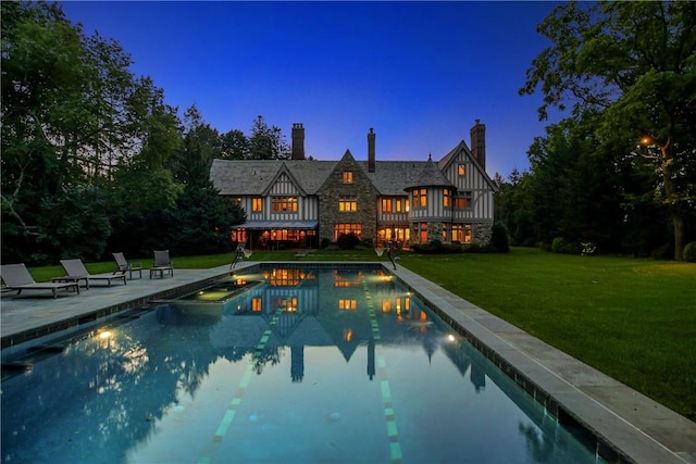 pool at dusk featuring a lawn and a patio area