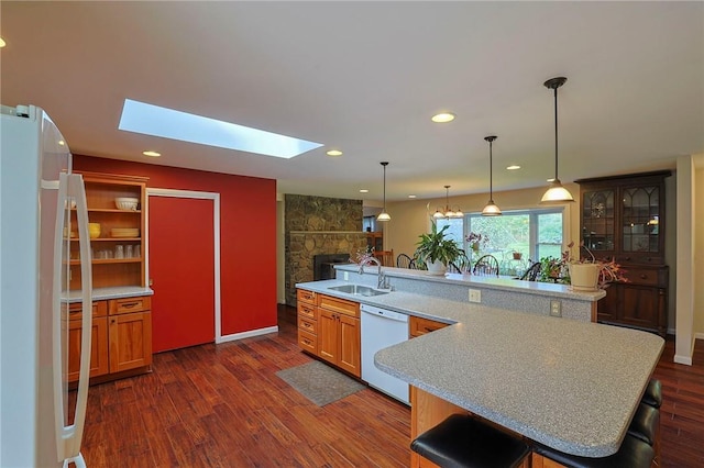 kitchen with a skylight, sink, dark hardwood / wood-style floors, white appliances, and a kitchen bar