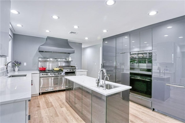 kitchen featuring light hardwood / wood-style floors, light stone countertops, wall chimney range hood, and sink