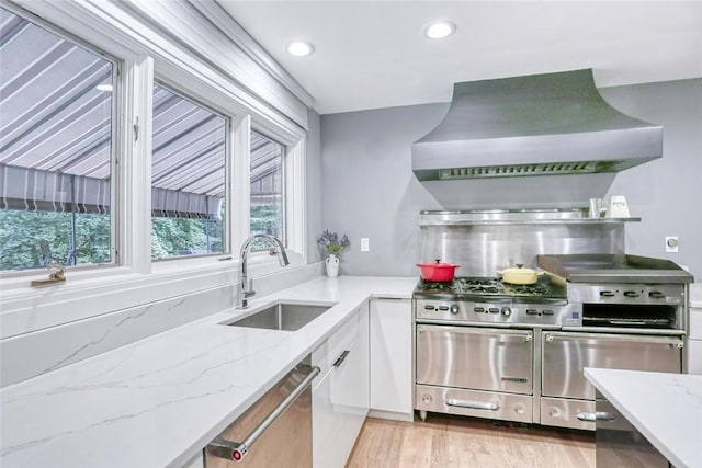 kitchen featuring light stone countertops, white cabinetry, sink, wall chimney exhaust hood, and stainless steel appliances