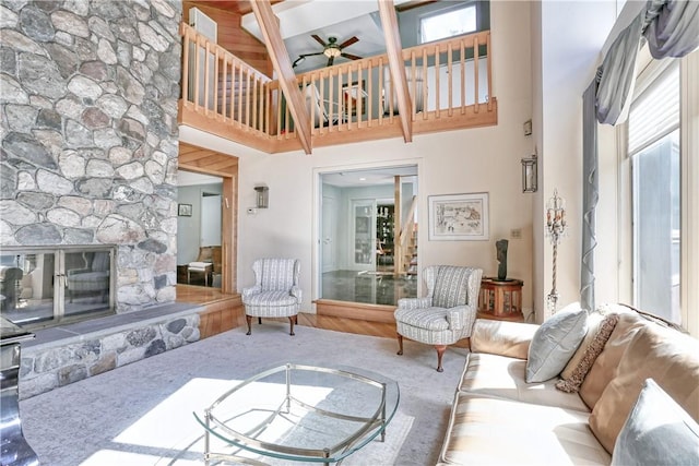 living room featuring ceiling fan, wood-type flooring, beamed ceiling, a high ceiling, and a stone fireplace