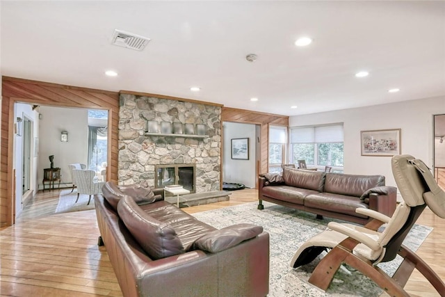 living room featuring wood walls, a stone fireplace, and light wood-type flooring