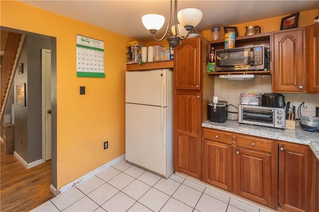 kitchen featuring light stone countertops, hanging light fixtures, an inviting chandelier, white refrigerator, and decorative backsplash