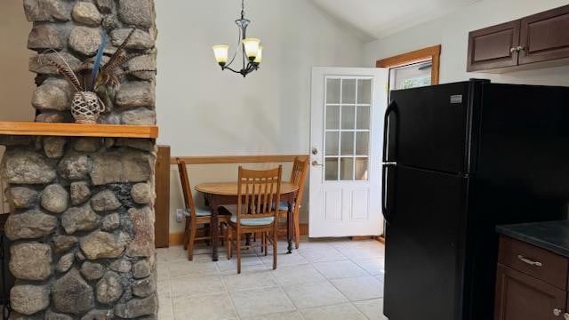 kitchen featuring dark brown cabinetry, a chandelier, vaulted ceiling, black refrigerator, and light tile patterned floors