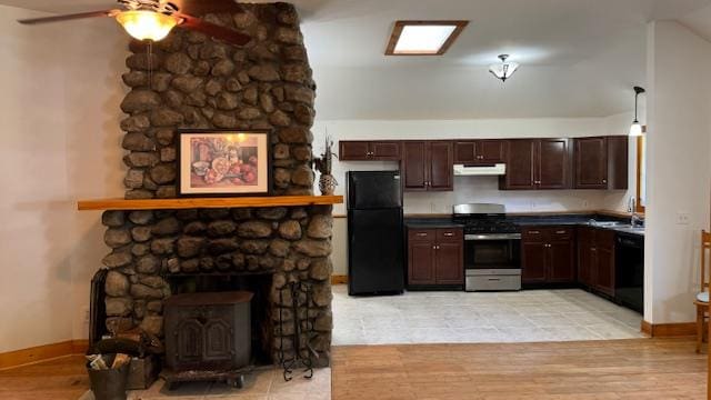 kitchen with a wood stove, black appliances, sink, light hardwood / wood-style flooring, and dark brown cabinetry