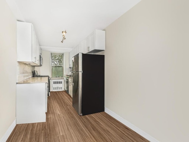 kitchen with hardwood / wood-style floors, decorative backsplash, white cabinetry, and stainless steel appliances