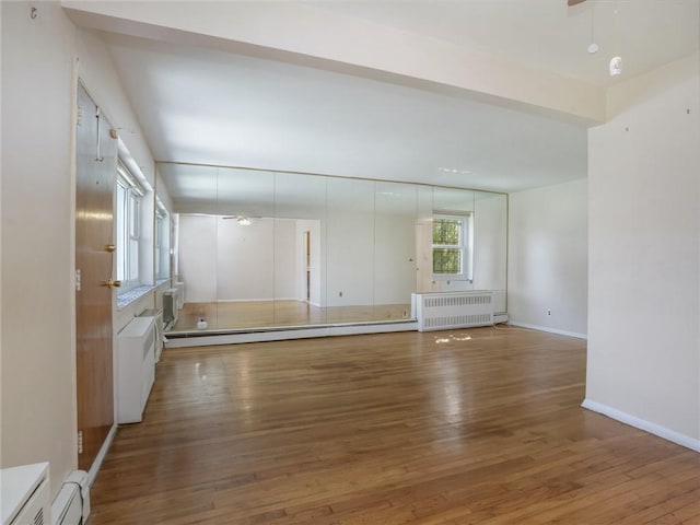 unfurnished living room featuring hardwood / wood-style floors, radiator, and a baseboard radiator