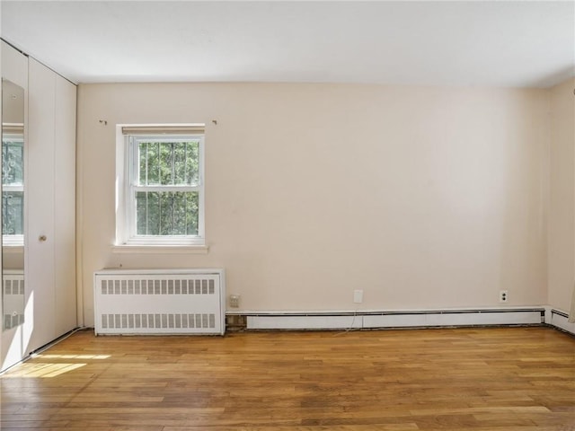 spare room with radiator heating unit, light wood-type flooring, and a baseboard heating unit