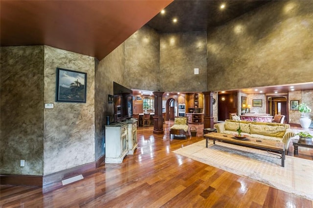 interior space featuring decorative columns, wood-type flooring, and a high ceiling