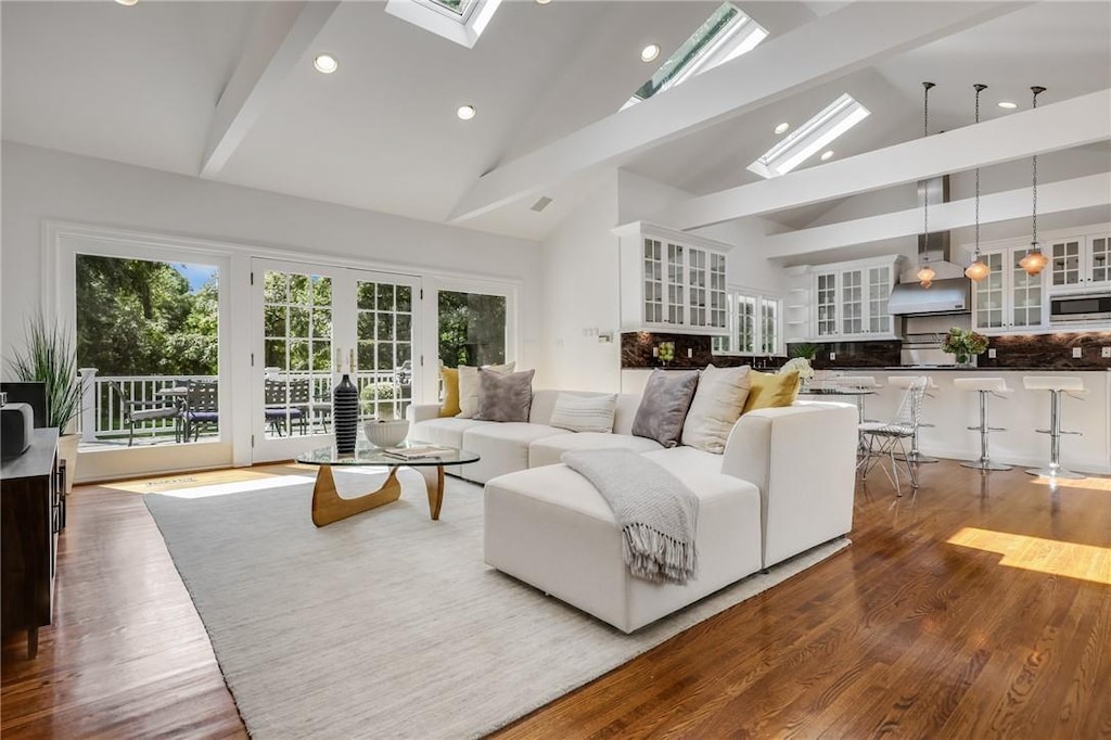 living room featuring hardwood / wood-style floors, high vaulted ceiling, french doors, a skylight, and beam ceiling