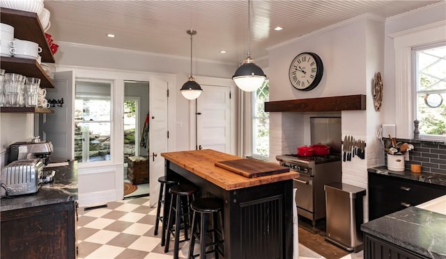 kitchen with a kitchen bar, tasteful backsplash, stainless steel range, exhaust hood, and decorative light fixtures