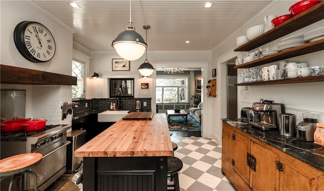 kitchen with high end range, wooden counters, ornamental molding, sink, and hanging light fixtures