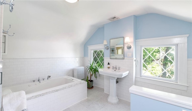 bathroom with tile patterned floors, vaulted ceiling, a relaxing tiled tub, tile walls, and radiator heating unit