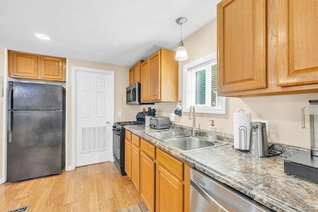 kitchen with black appliances, light wood-type flooring, sink, and hanging light fixtures