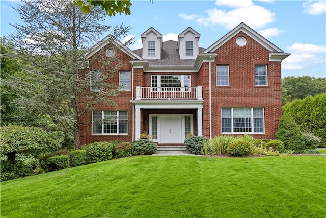 colonial inspired home featuring a balcony, brick siding, and a front yard