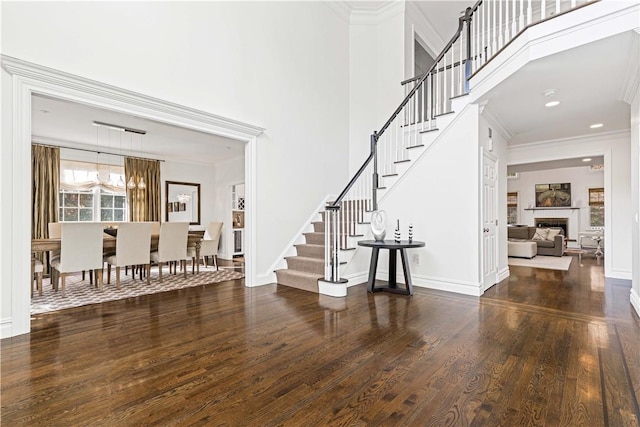 foyer with a fireplace, stairway, dark wood-type flooring, and crown molding