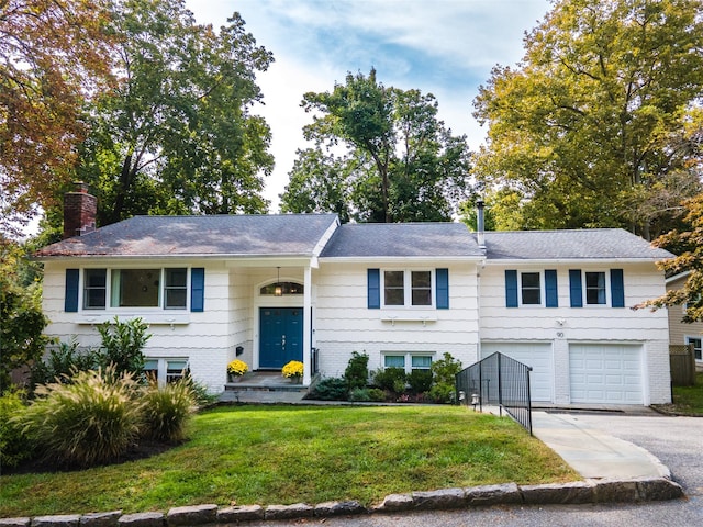 split foyer home with driveway, a front yard, a garage, brick siding, and a chimney