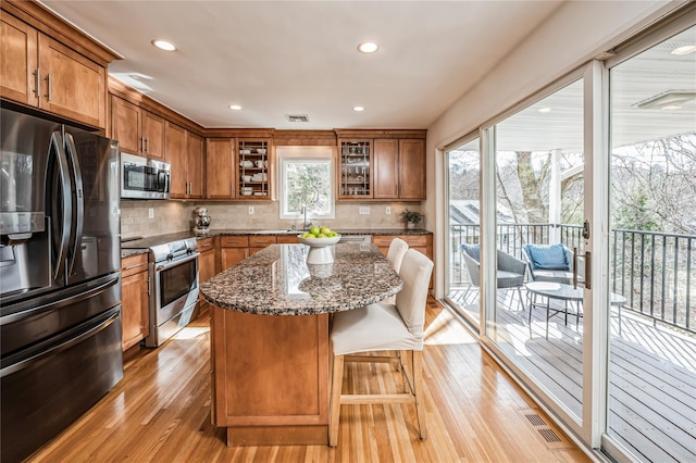 kitchen with dark stone countertops, a center island, brown cabinetry, and stainless steel appliances