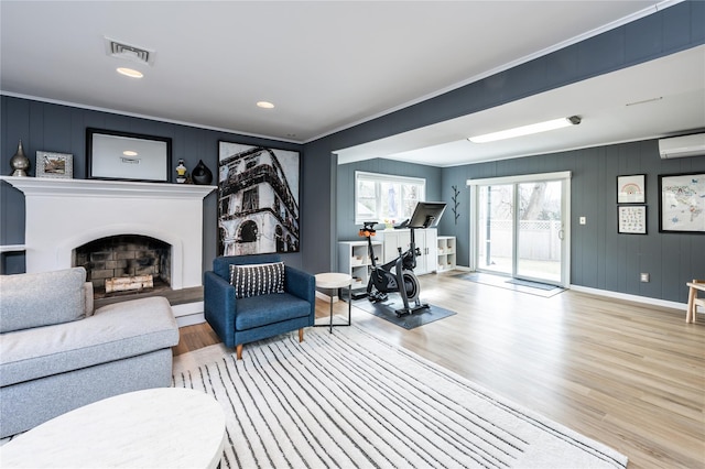 living room with visible vents, crown molding, a wall mounted air conditioner, a fireplace, and wood finished floors