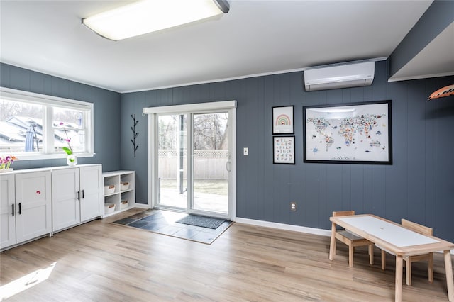 doorway featuring light wood finished floors, plenty of natural light, a wall mounted air conditioner, and baseboards