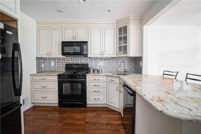 kitchen featuring light stone countertops, sink, a kitchen breakfast bar, dark hardwood / wood-style flooring, and black appliances