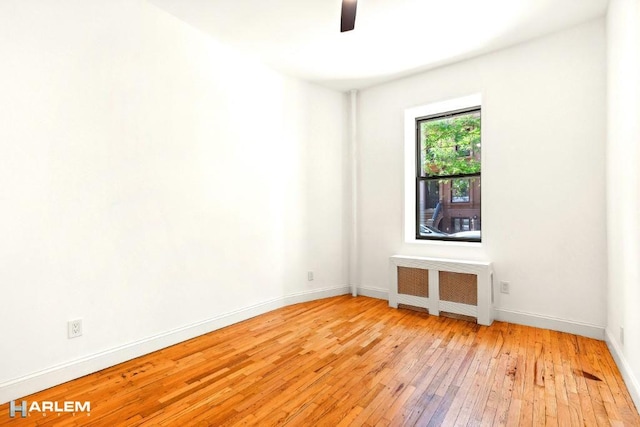 empty room featuring radiator heating unit, light hardwood / wood-style flooring, and ceiling fan