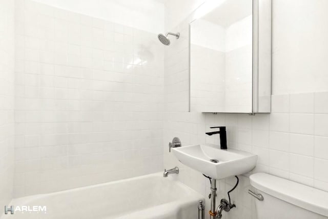 full bathroom with sink, tiled shower / bath combo, tile walls, and toilet