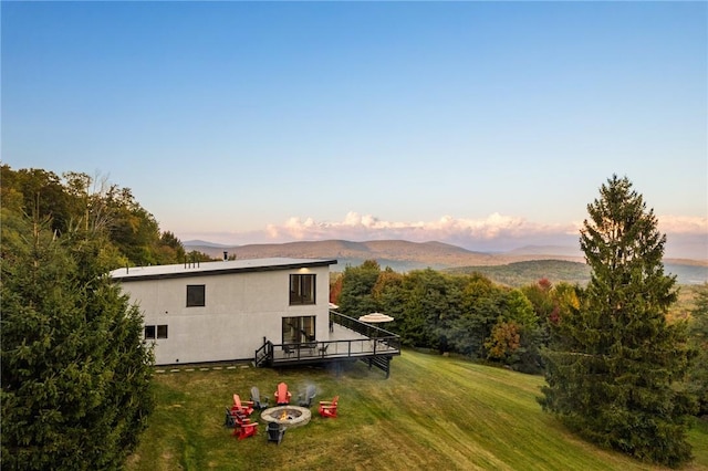 back house at dusk featuring a deck with mountain view, an outdoor fire pit, and a lawn