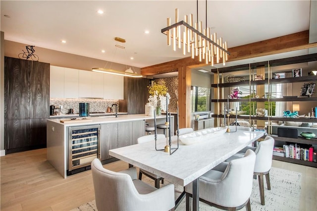 dining space featuring beamed ceiling, light wood-type flooring, and beverage cooler