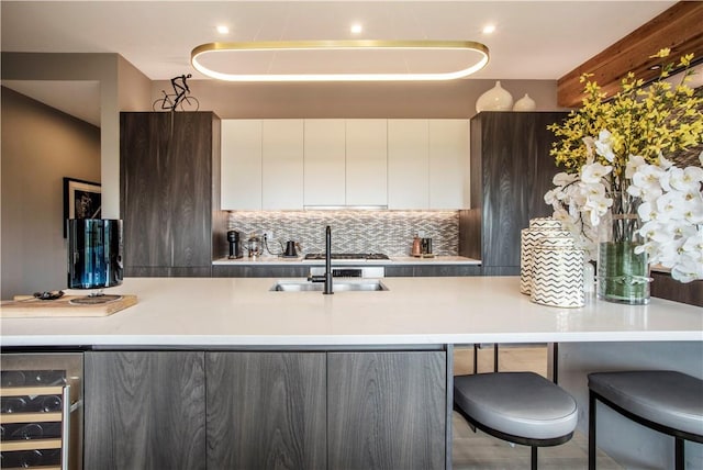 kitchen with white cabinetry, sink, wine cooler, a kitchen bar, and decorative backsplash