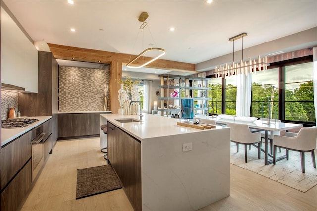 kitchen featuring hanging light fixtures, light hardwood / wood-style flooring, a kitchen island with sink, and sink