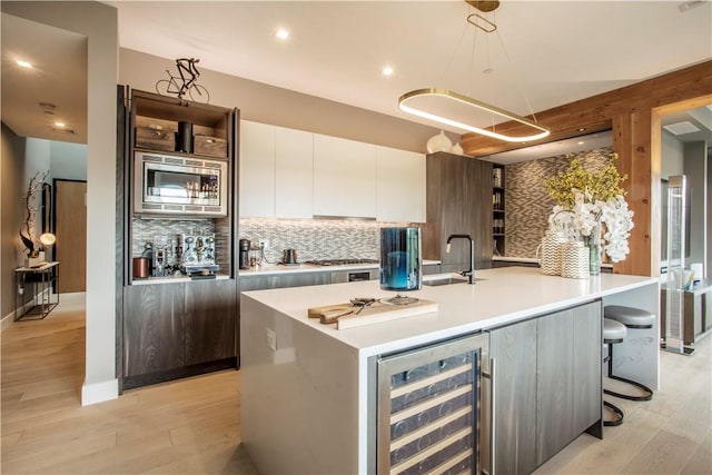 kitchen with sink, stainless steel microwave, beverage cooler, white cabinets, and light wood-type flooring