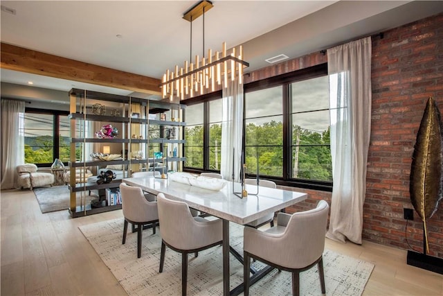 dining area with brick wall, light hardwood / wood-style floors, a wealth of natural light, and a chandelier