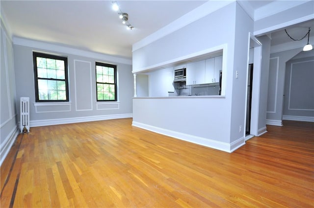 unfurnished living room featuring radiator, light hardwood / wood-style flooring, and track lighting