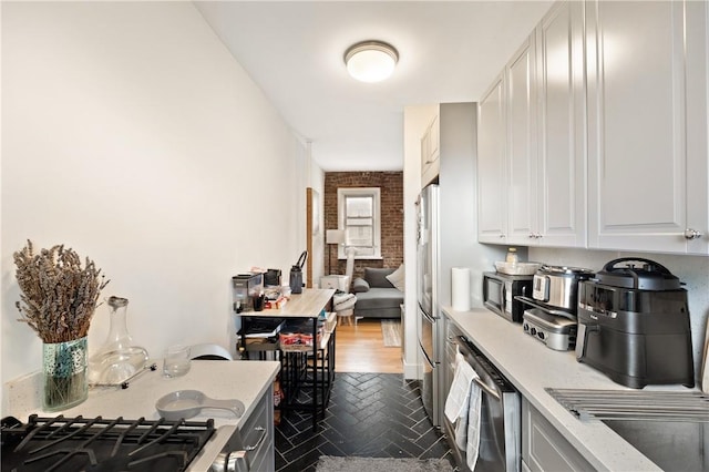 kitchen featuring dark hardwood / wood-style floors, white cabinetry, stainless steel appliances, and brick wall