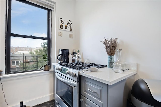 kitchen with gray cabinets, light stone counters, and stainless steel range