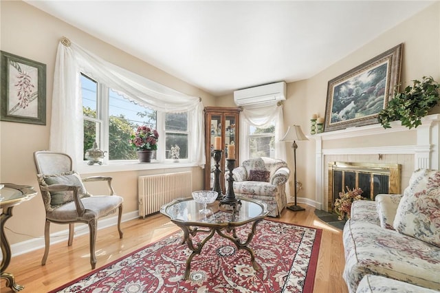 sitting room featuring a tiled fireplace, radiator heating unit, hardwood / wood-style floors, and a wall mounted air conditioner