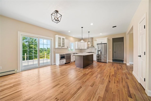 kitchen with white cabinetry, a center island, hanging light fixtures, stainless steel appliances, and wall chimney range hood