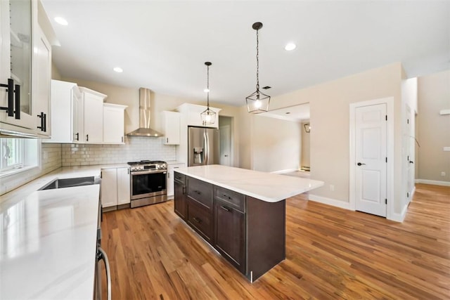 kitchen with a center island, white cabinets, wall chimney exhaust hood, light wood-type flooring, and stainless steel appliances