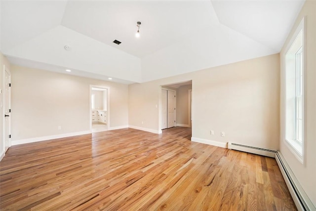 empty room featuring vaulted ceiling, light wood-type flooring, and a baseboard heating unit