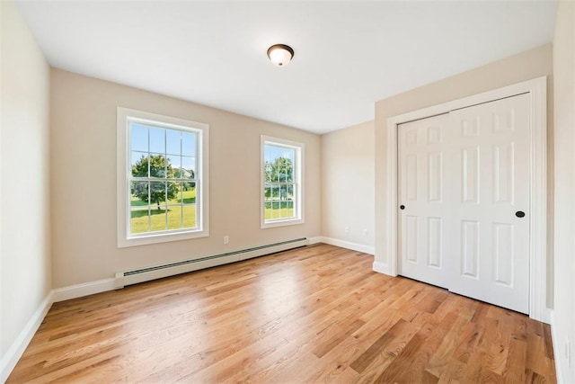 unfurnished bedroom featuring baseboard heating, a closet, and light hardwood / wood-style floors