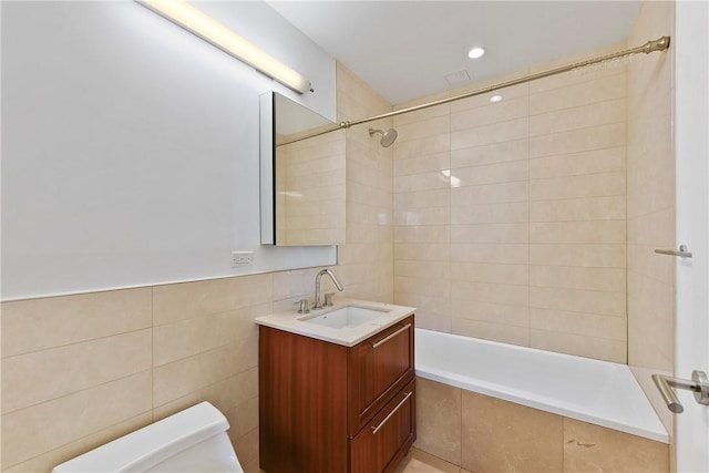 full bathroom featuring tiled shower / bath combo, toilet, tile walls, and vanity