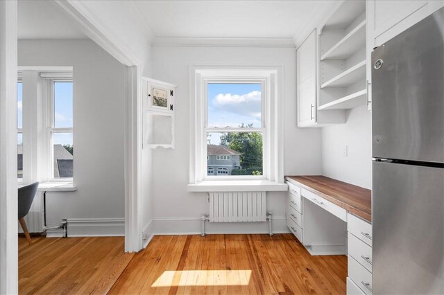 interior space featuring radiator, ornamental molding, built in desk, and light wood-type flooring