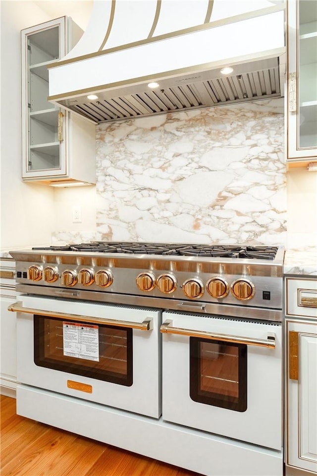 kitchen featuring custom exhaust hood, double oven range, white cabinets, light hardwood / wood-style flooring, and light stone countertops