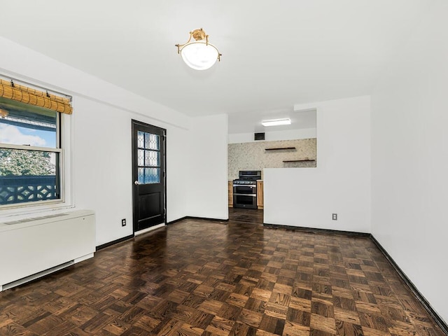 unfurnished living room with radiator, a wealth of natural light, and dark parquet flooring