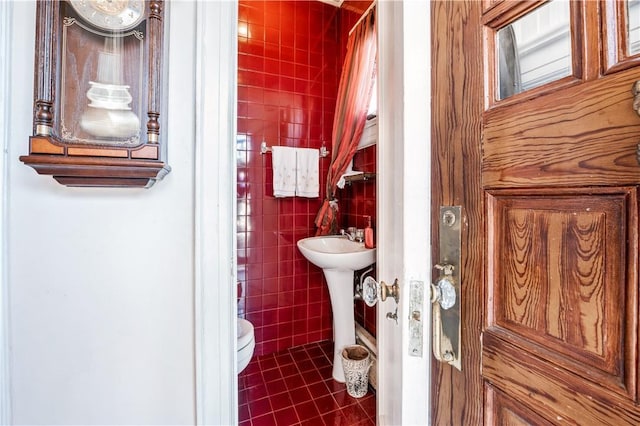 bathroom with toilet, tile patterned floors, and tile walls