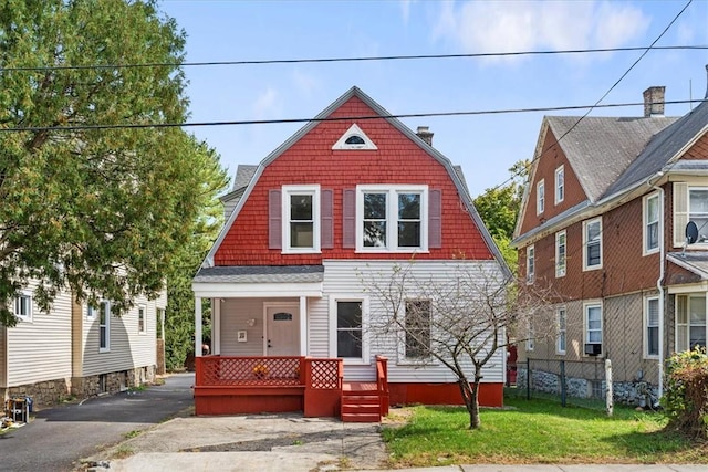 view of front of home with fence, a front lawn, a gambrel roof, and a porch