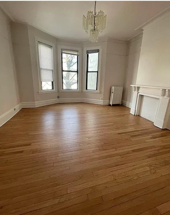 interior space with hardwood / wood-style floors, a notable chandelier, radiator heating unit, and crown molding