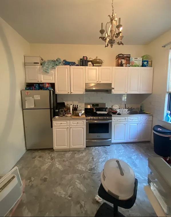 3216 31st Ave, Astoria, NY 11106 - kitchen with freestanding refrigerator, stainless steel range with gas stovetop, under cabinet range hood, a chandelier, and white cabinetry