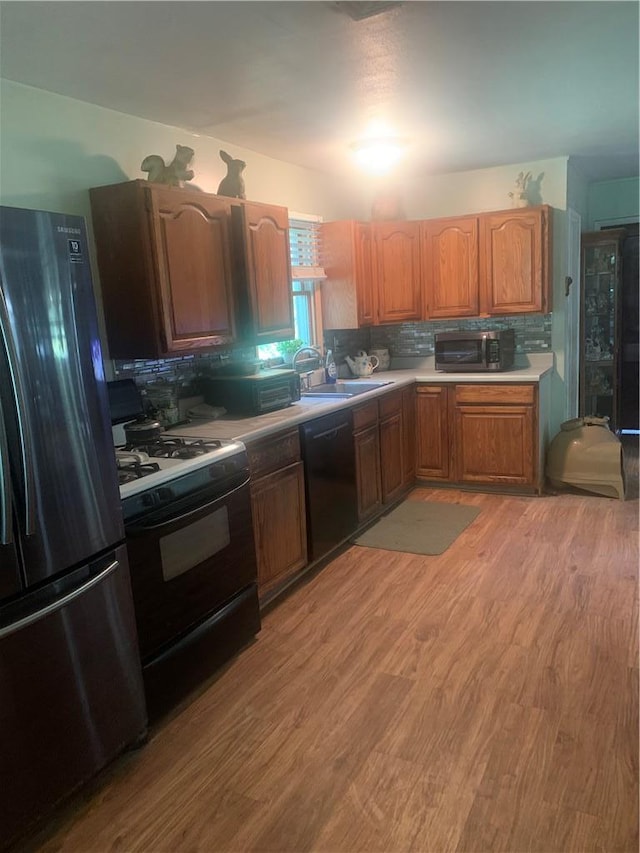 kitchen with sink, backsplash, light hardwood / wood-style floors, and black appliances